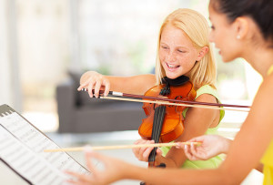 Young girl learning to play violin from a music instructor.