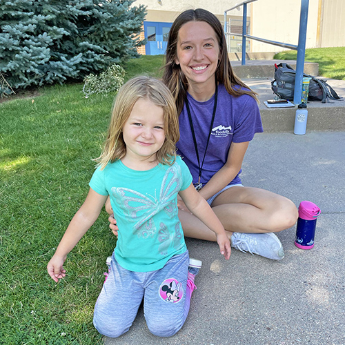 Summer Camp Leader posing with a smiling, little girl.