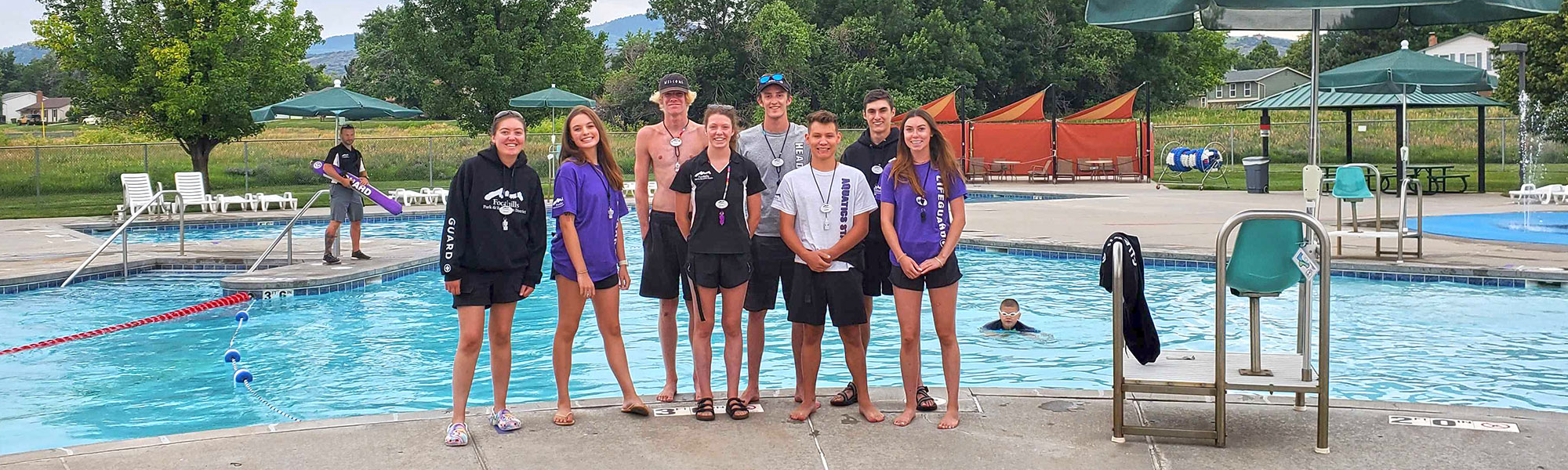 Group of lifeguards standing in front of an outdoor pool.