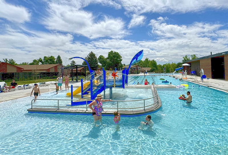Columbine West Outdoor Pool site showing people playing in the water and on a water play structure.