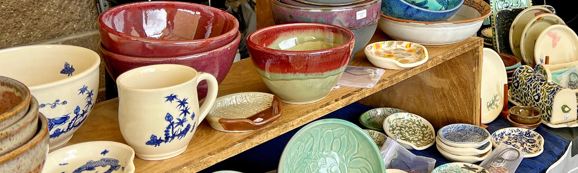 A variety of colorful pottery pieces like bowls, mugs and spoon rests displayed at a pottery sale.