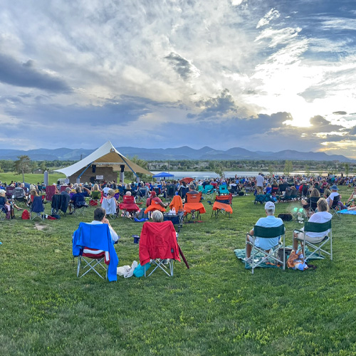 Concert goers enjoying a live summer concert on the amphitheater with mountain views in the background.