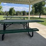 Two picnic tables under a park shelter with mountain views in the background.