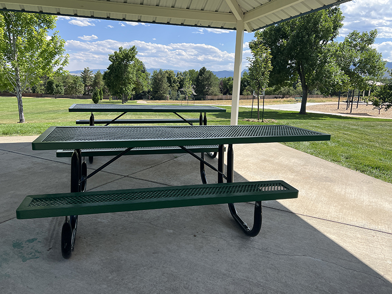 Two picnic tables under a park shelter with mountain views in the background.