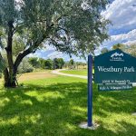 Park entrance sign reading Westbury Park with a meandering sidewalk trail.