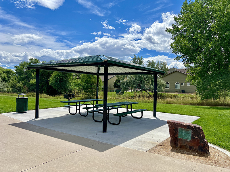 A park shelter with picnic tables and a memorial rock beside it.