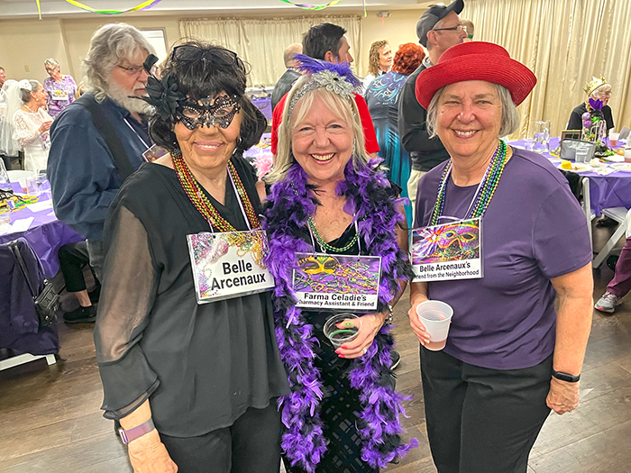 Three woman grouped together dressed in Mardi Gras theme for a murder mystery dinner.