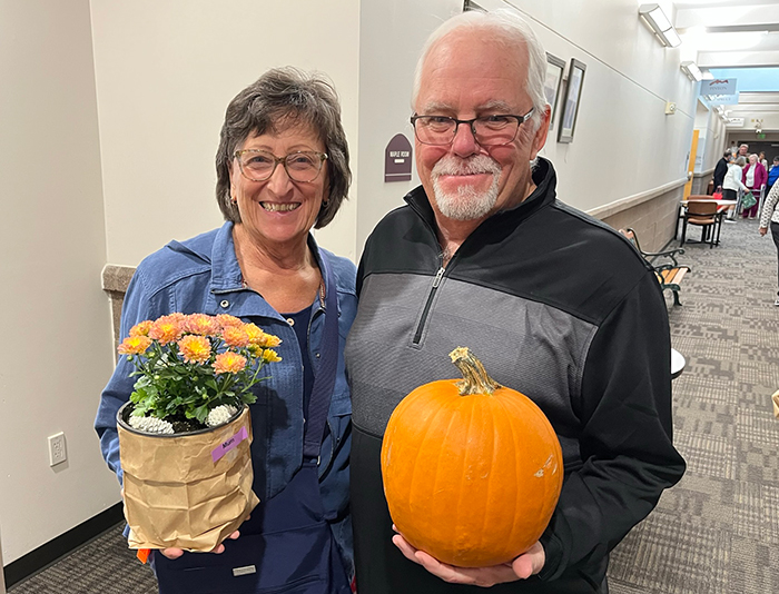 A woman holding a mum plant and a man holding a pumpkin.