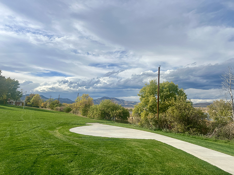 Park view of green grass, a sidewalk trail and mountains in the background.