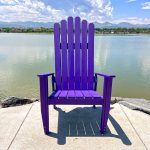 Oversized purple adirondack chair near a body of water with mountains in the background.