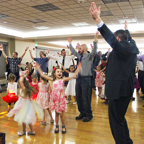 Little girls and their fathers dancing at an event.