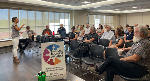 Woman giving presentation to South Jeffco Business Alliance meeting attendees.